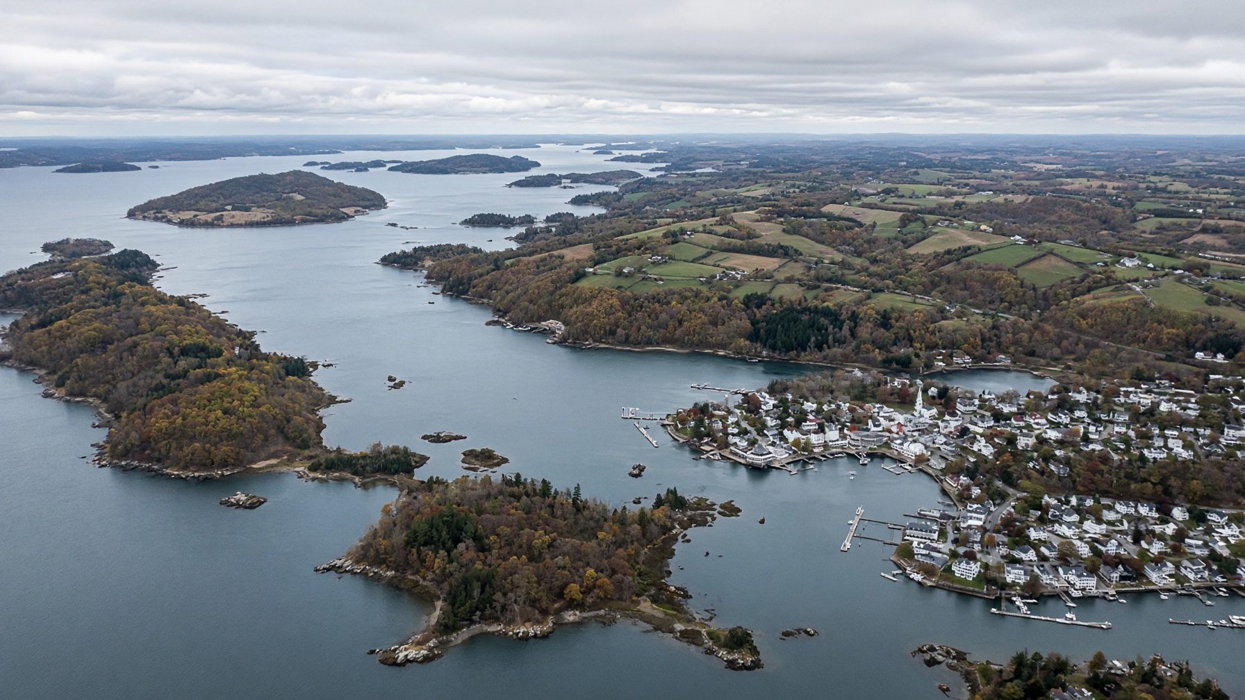 Aerial view of a bay with wooded islands, a harbor town with boats, and farmland