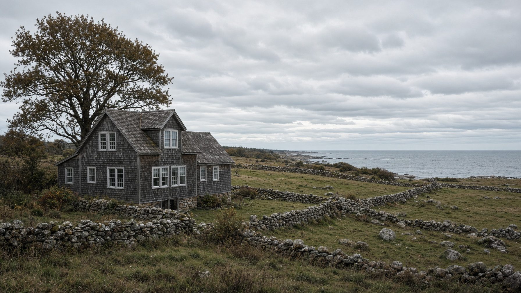 Gray-shingled farmhouse among fieldstone walls in an open field running down to the ocean