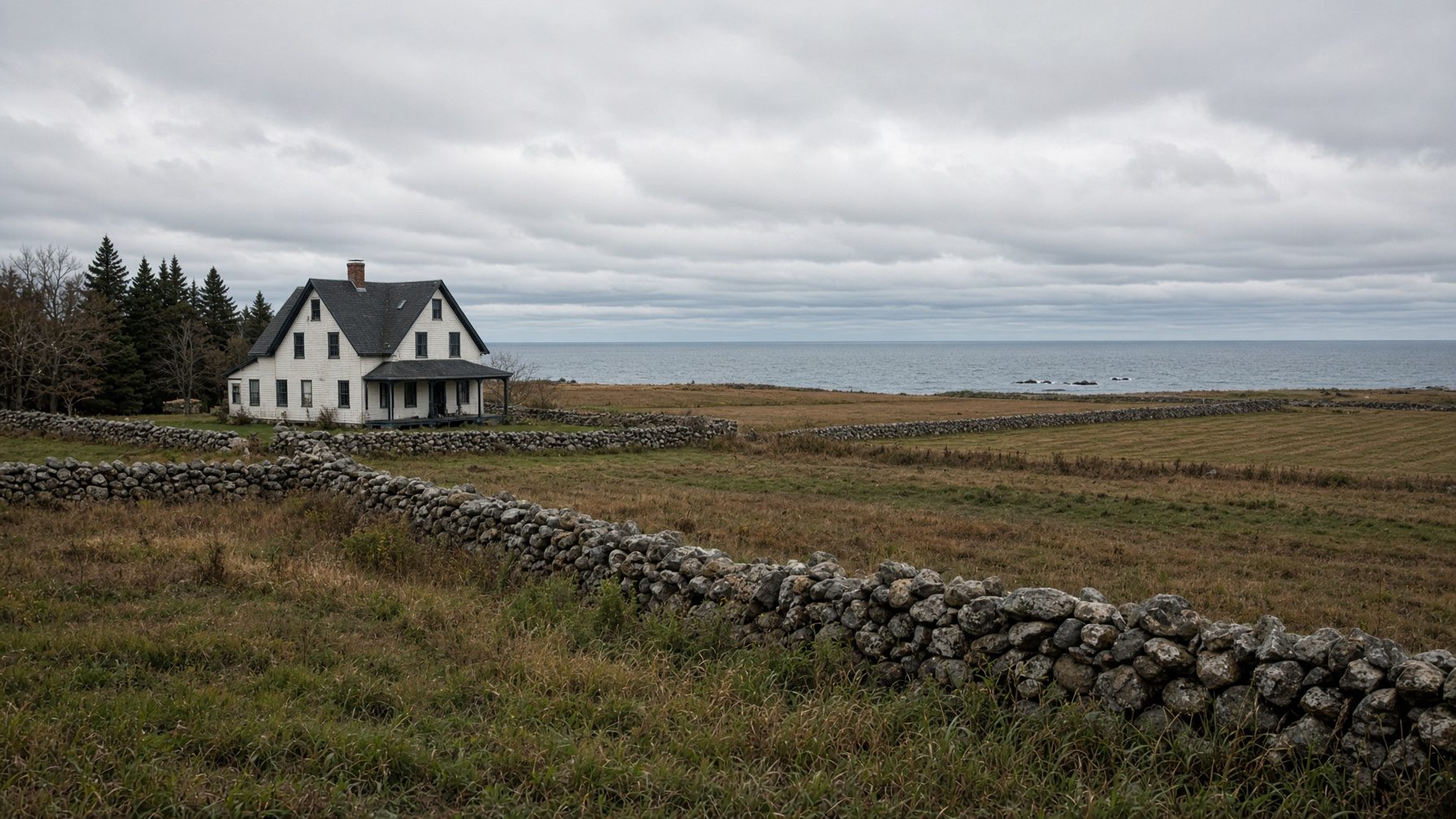 White farmhouse at the edge of a field lined with stone walls, with the ocean on the horizon