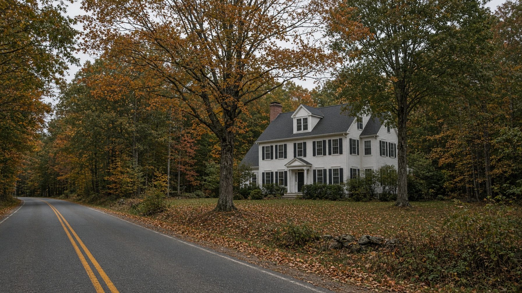 White colonial with dormers set back in the woods along a two-lane country road